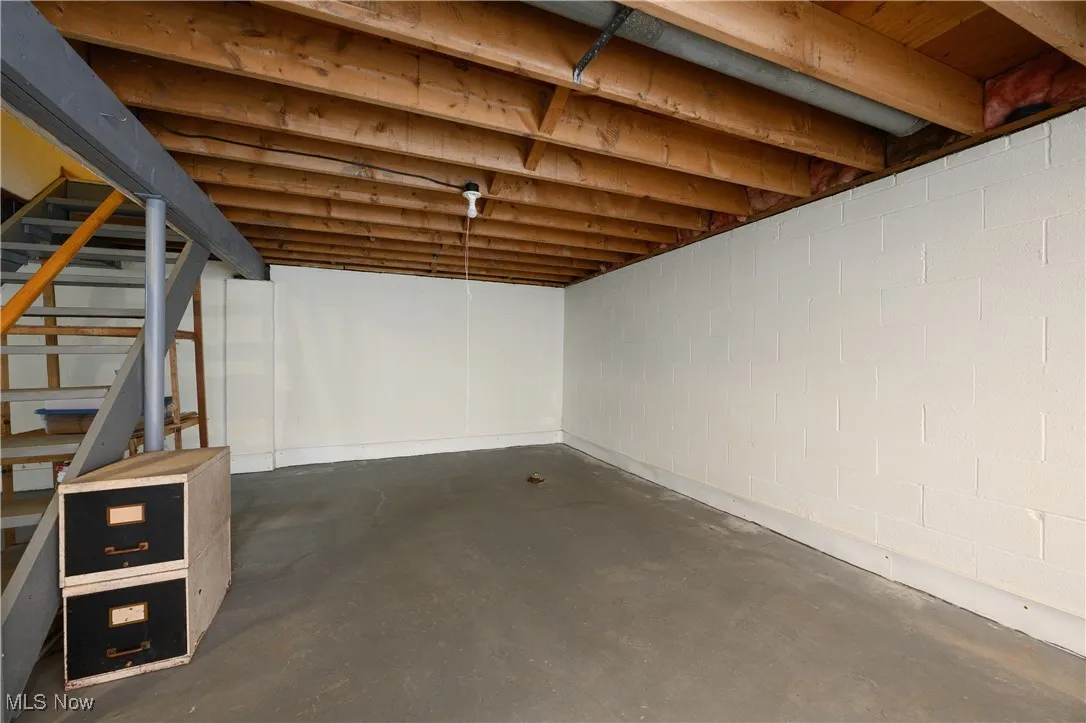 Unfinished basement with concrete block wall and stairway