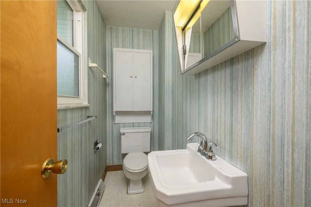Bathroom with wallpapered walls and speckled floor
