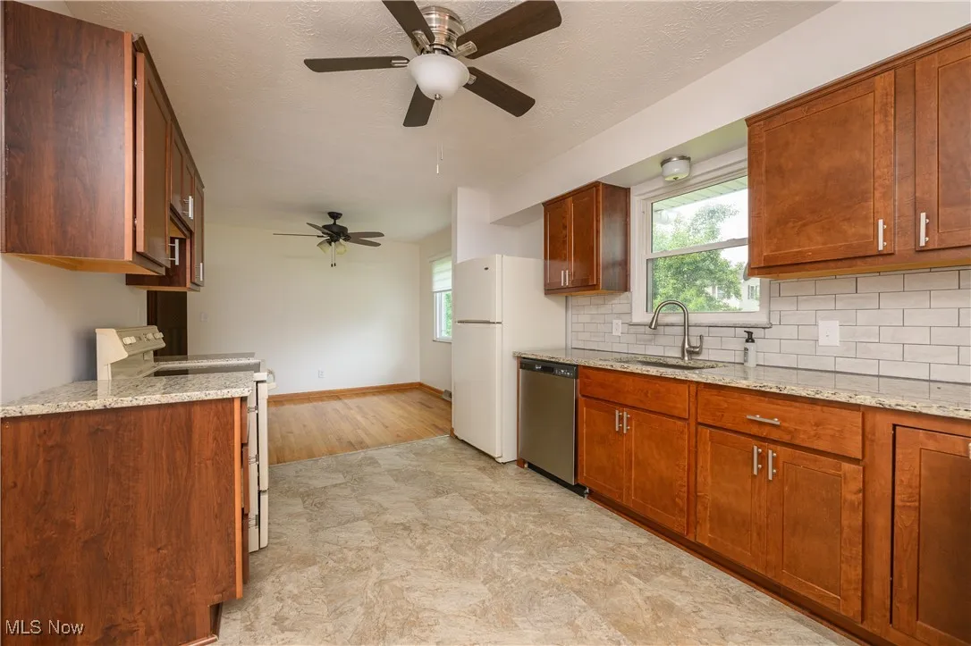 Kitchen featuring white appliances, decorative backsplash, a ceiling fan, light stone counters, and light floors