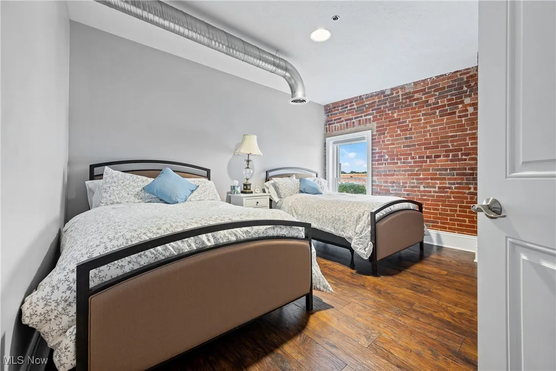 Bedroom featuring brick wall and wood finished floors