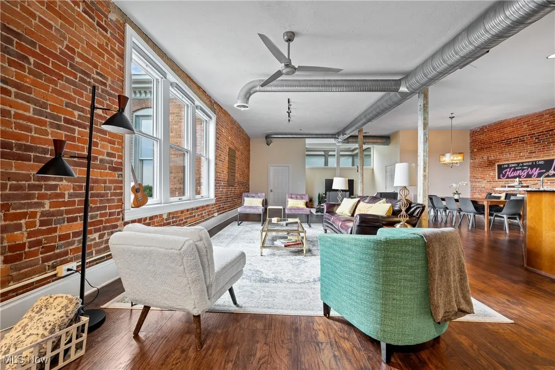 Living area with brick wall, wood finished floors, and ceiling fan