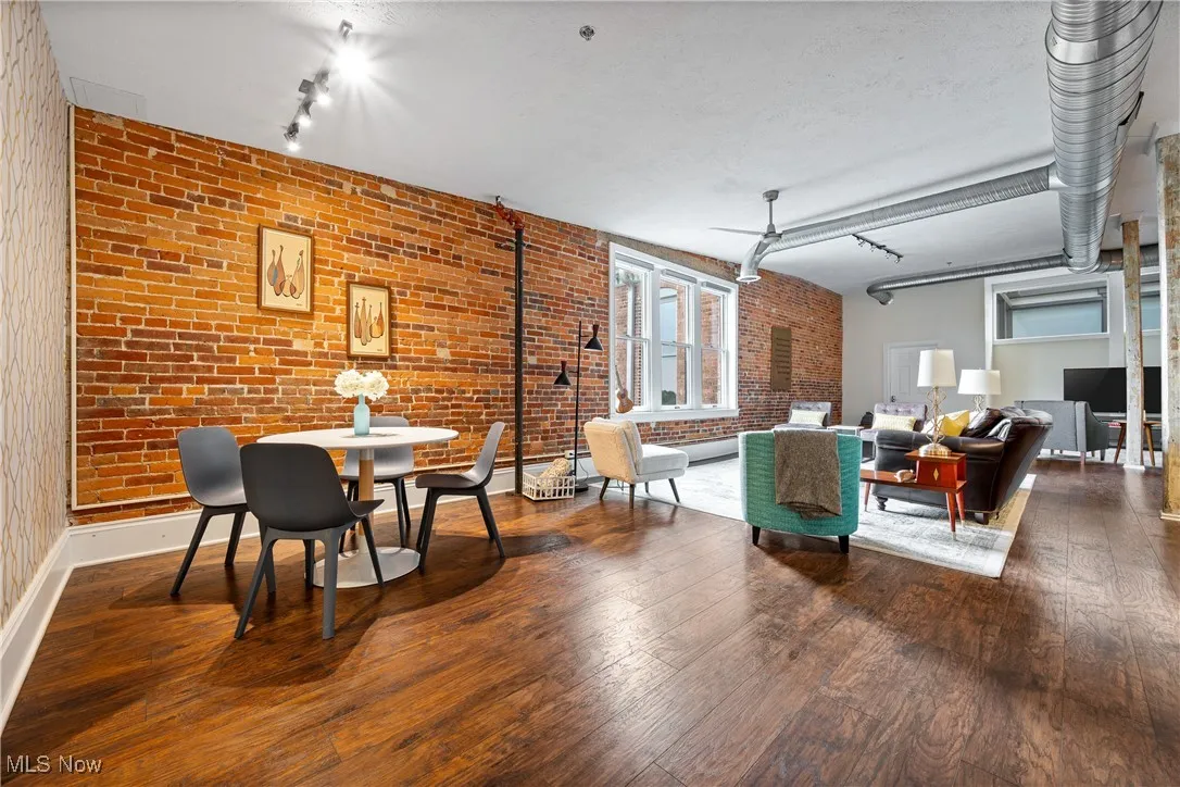 Dining room with rail lighting, wood-type flooring, and brick wall