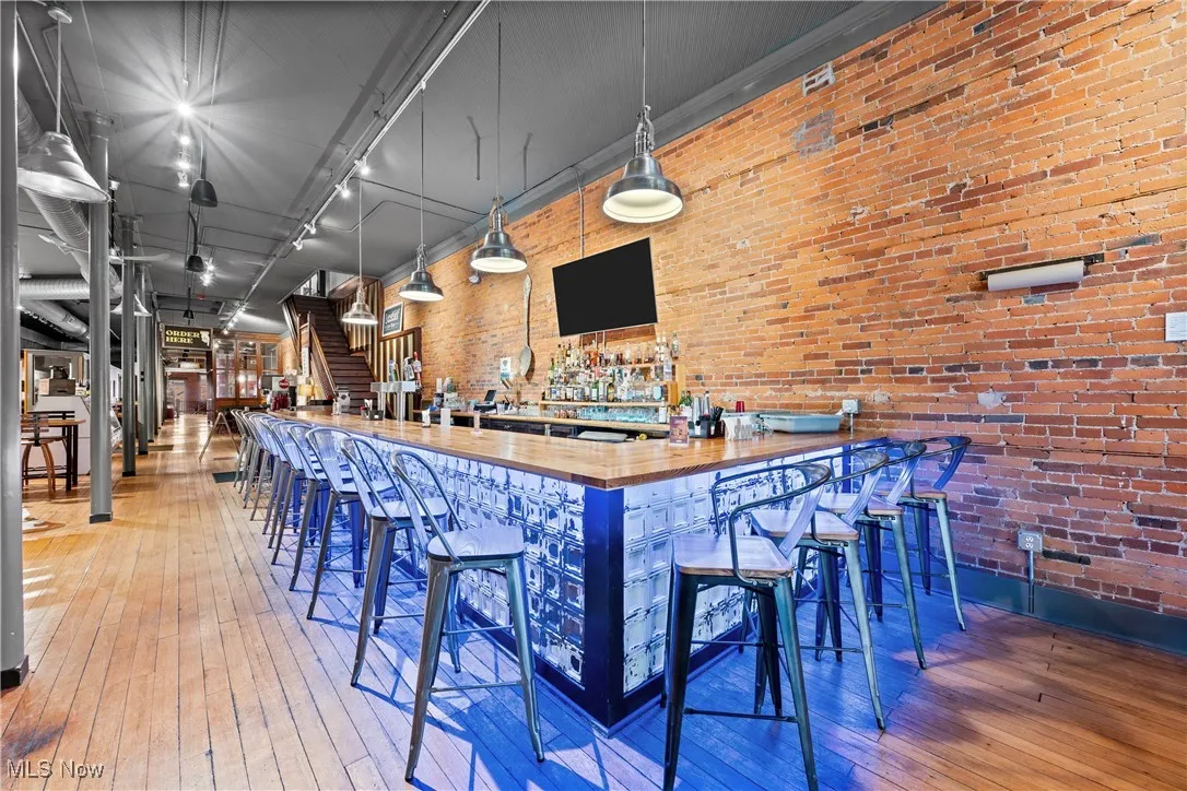 Community bar area with hardwood / wood-style floors, brick wall, and rail lighting