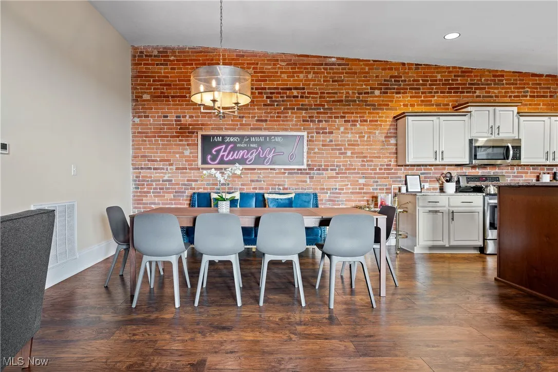 Dining room with dark wood-style floors, brick wall, and recessed lighting