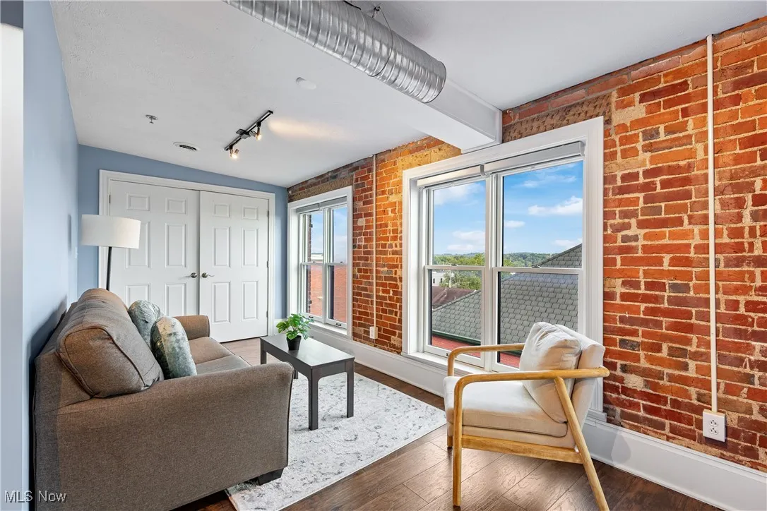 Living room with brick wall, wood finished floors, and rail lighting