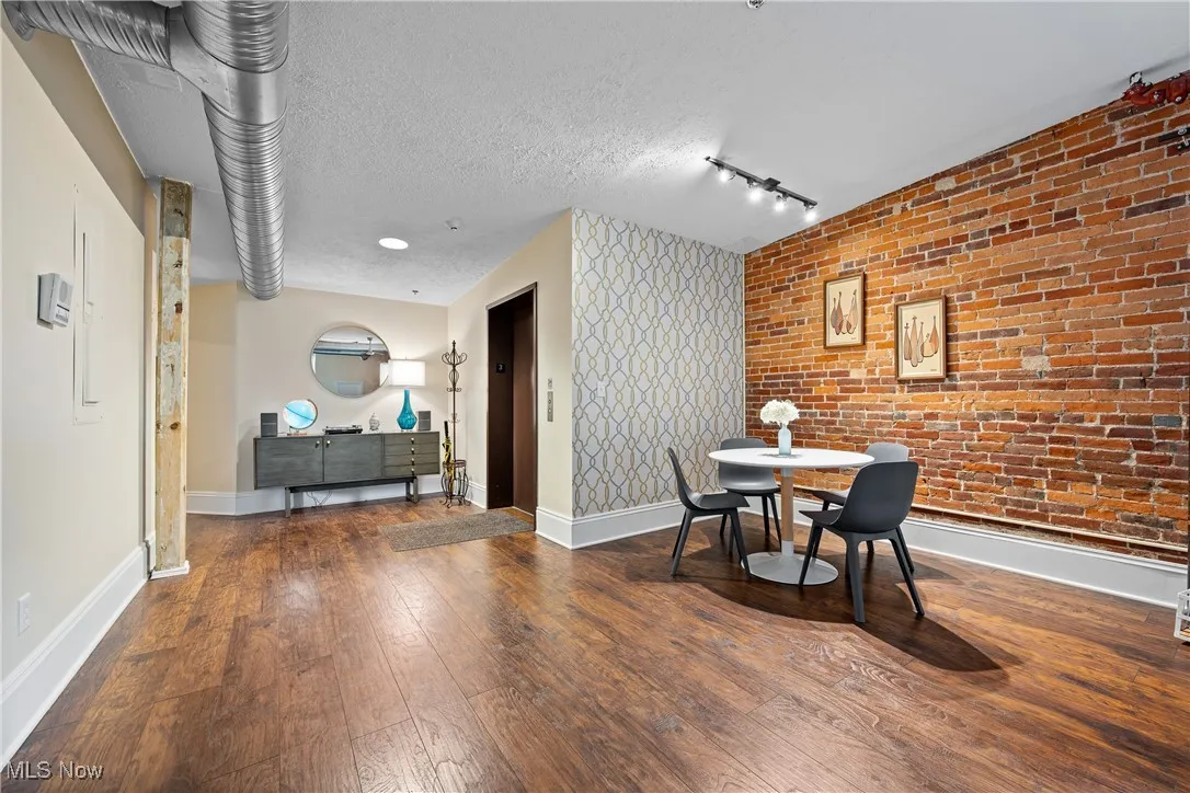 Dining space featuring hardwood / wood-style flooring, an accent wall, elevator, brick wall, and track lighting