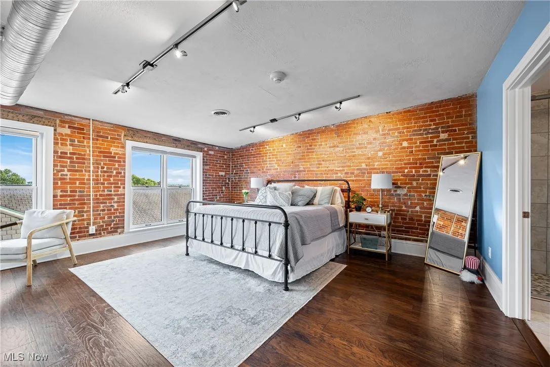 Bedroom featuring track lighting, brick wall, and wood finished floors