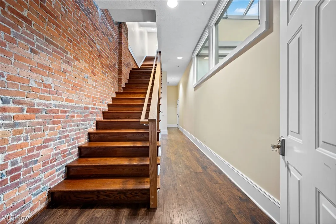 Stairway featuring brick wall, wood-type flooring, and recessed lighting