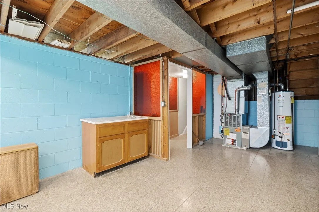 Unfinished basement with light flooring, heating unit, and gas water heater