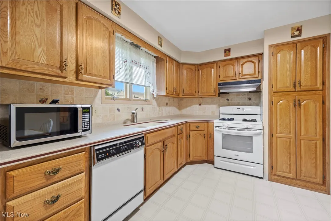 Kitchen with white appliances, light countertops, light flooring, under cabinet range hood, and tasteful backsplash