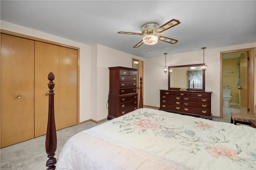 Bedroom featuring light carpet, a closet, ensuite bath, and ceiling fan
