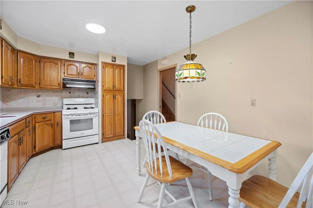 Kitchen with white range with gas cooktop, brown cabinetry, backsplash, and under cabinet range hood