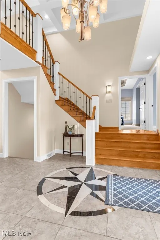 Foyer, featuring stairway with a chandelier, recessed lighting, a towering ceiling, and inlaid floor details