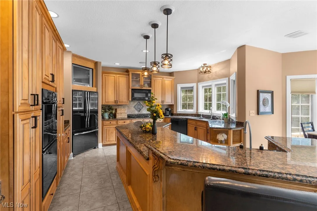 Kitchen featuring tasteful backsplash, black appliances, maple cabinets, ceramic tile floors, and granite countertops