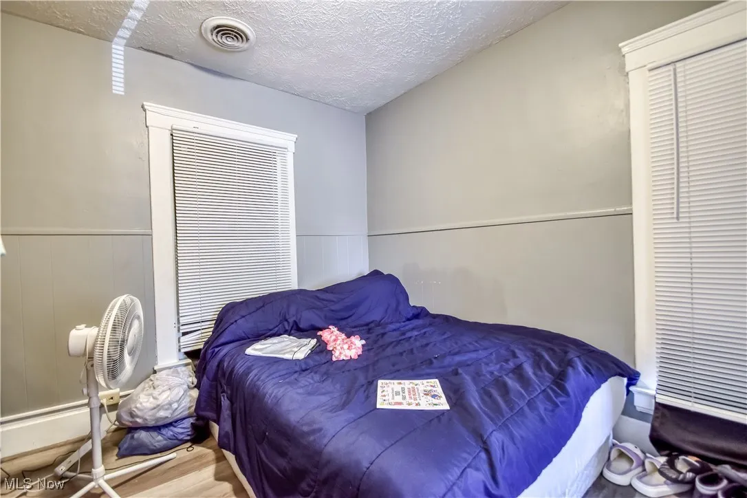 Bedroom featuring a textured ceiling, a wainscoted wall, and wood finished floors