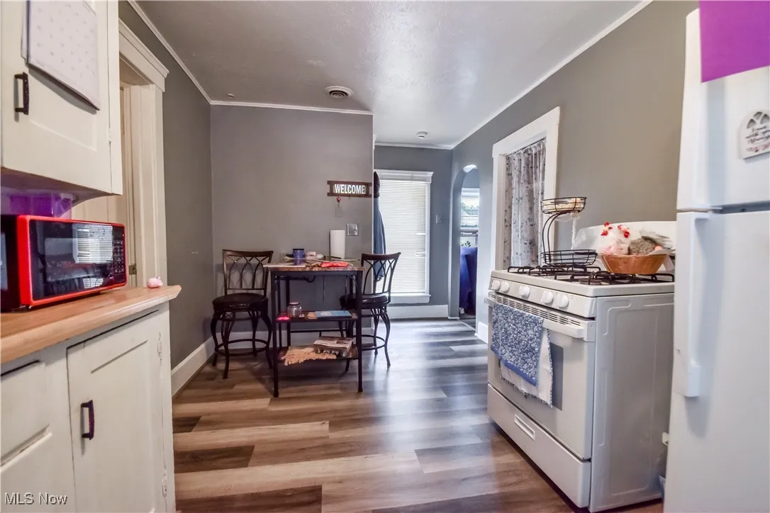 Kitchen featuring white appliances, crown molding, white cabinets, and wood finished floors