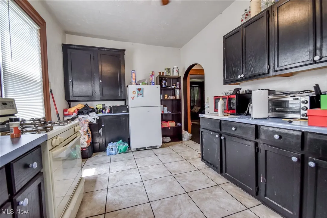 Kitchen featuring white appliances, arched walkways, light countertops, and light tile patterned flooring