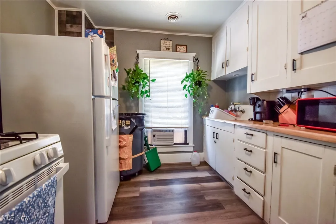 Kitchen featuring white range with gas cooktop, white cabinets, dark wood finished floors, light countertops, and crown molding