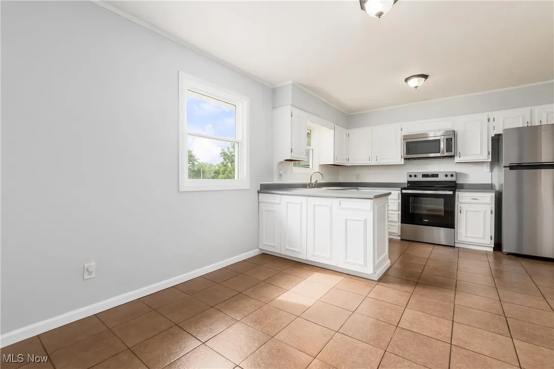 Kitchen with appliances with stainless steel finishes, light tile patterned floors, white cabinetry, ornamental molding, and a peninsula