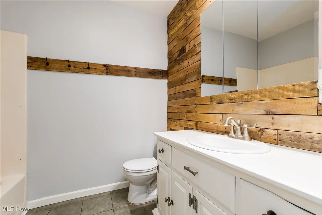 Bathroom with tile patterned floors, vanity, and wood walls