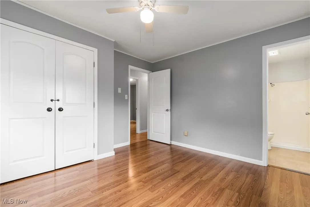 Unfurnished bedroom featuring crown molding, a closet, light wood-style flooring, ensuite bath, and a ceiling fan