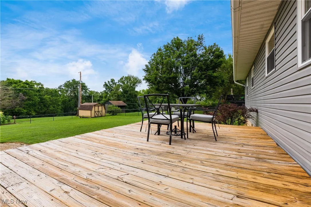Deck with outdoor dining space, a shed, and view of scattered trees