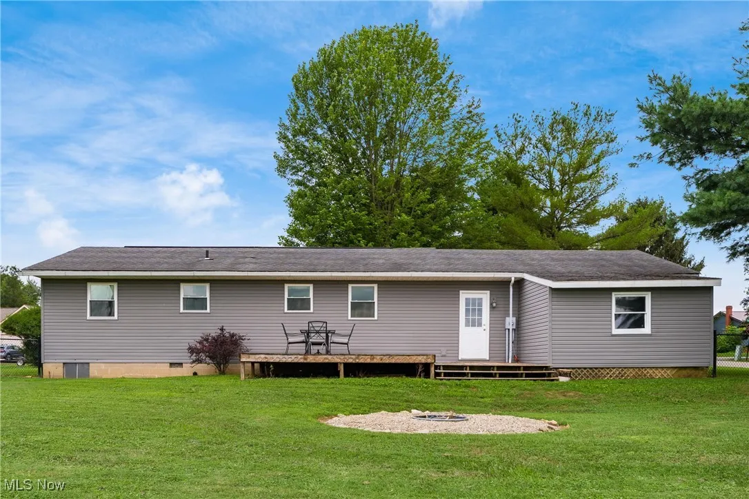 Rear view of house with crawl space, a wooden deck, a lawn, and a fire pit