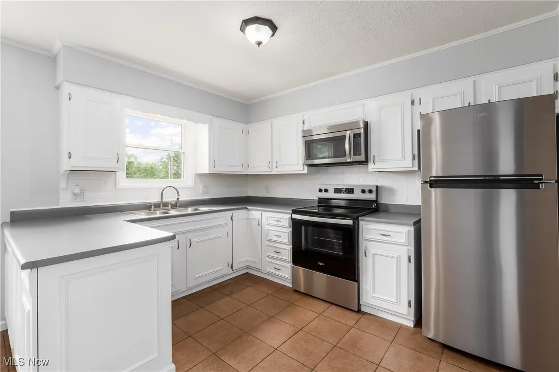 Kitchen with appliances with stainless steel finishes, backsplash, crown molding, white cabinetry, and tile patterned flooring