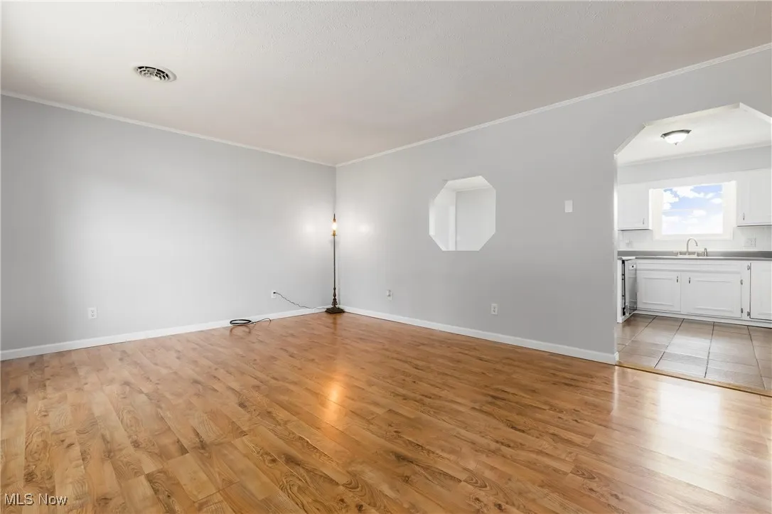 Empty room with ornamental molding, light wood-style flooring, and arched walkways