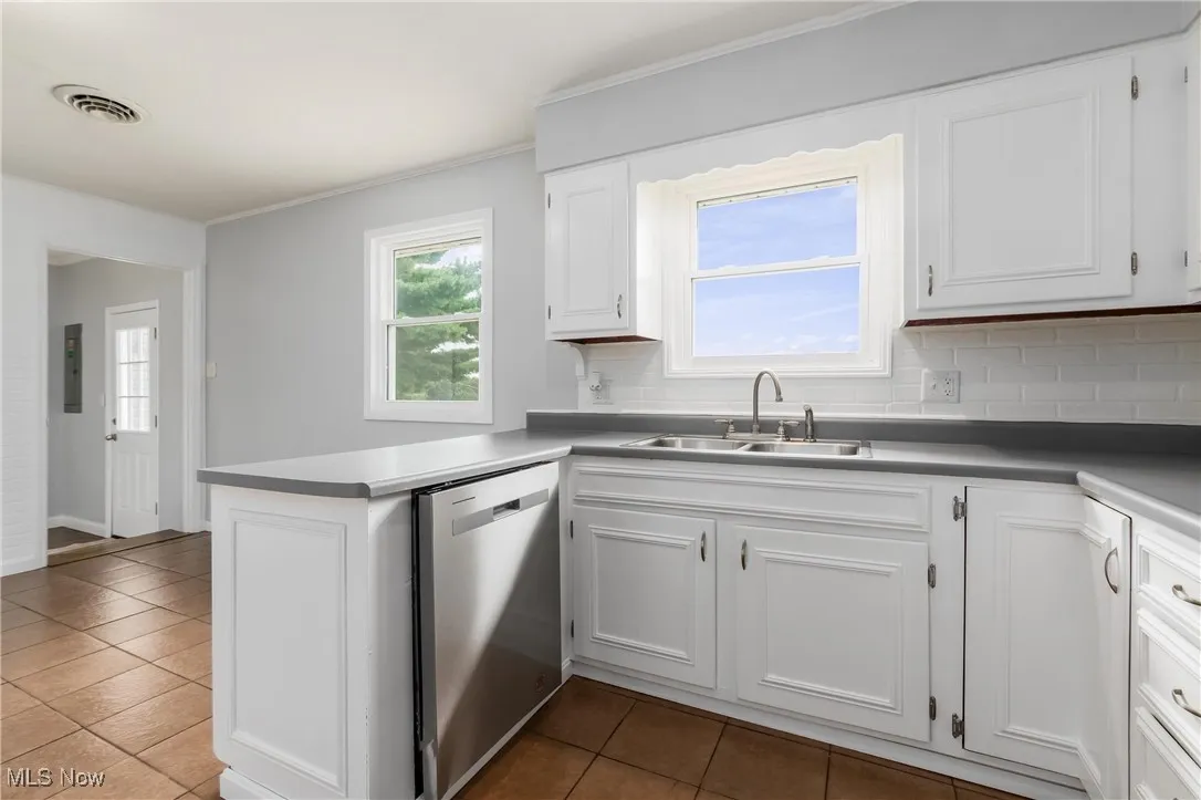 Kitchen with tile patterned flooring, stainless steel dishwasher, tasteful backsplash, white cabinets, and crown molding