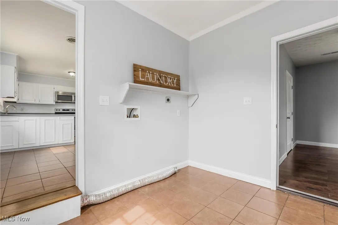 Washroom with electric dryer hookup, crown molding, washer hookup, and light tile patterned floors