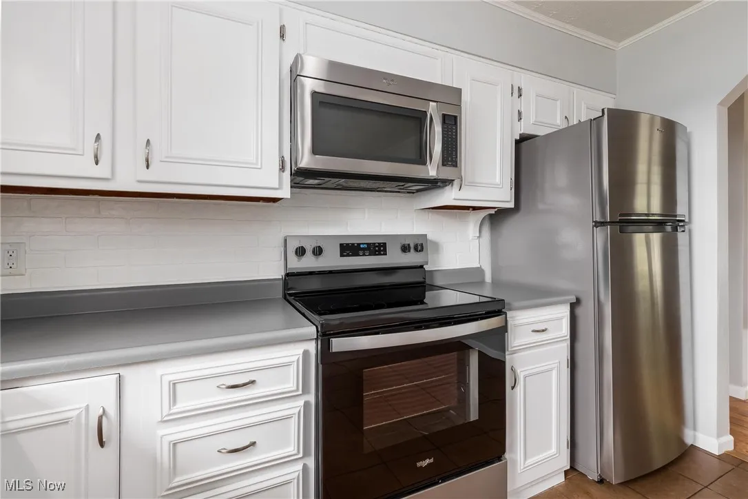 Kitchen with stainless steel appliances, crown molding, tasteful backsplash, and white cabinetry