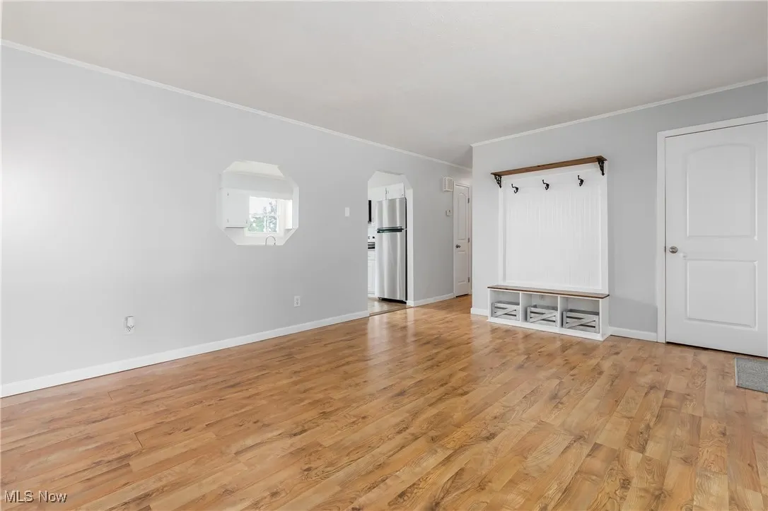 Unfurnished living room with crown molding, light wood-style flooring, and arched walkways