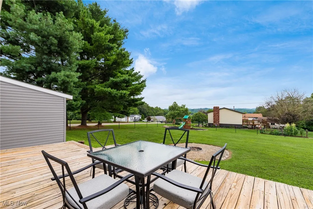 Wooden deck featuring outdoor dining area, a playground, and a lawn