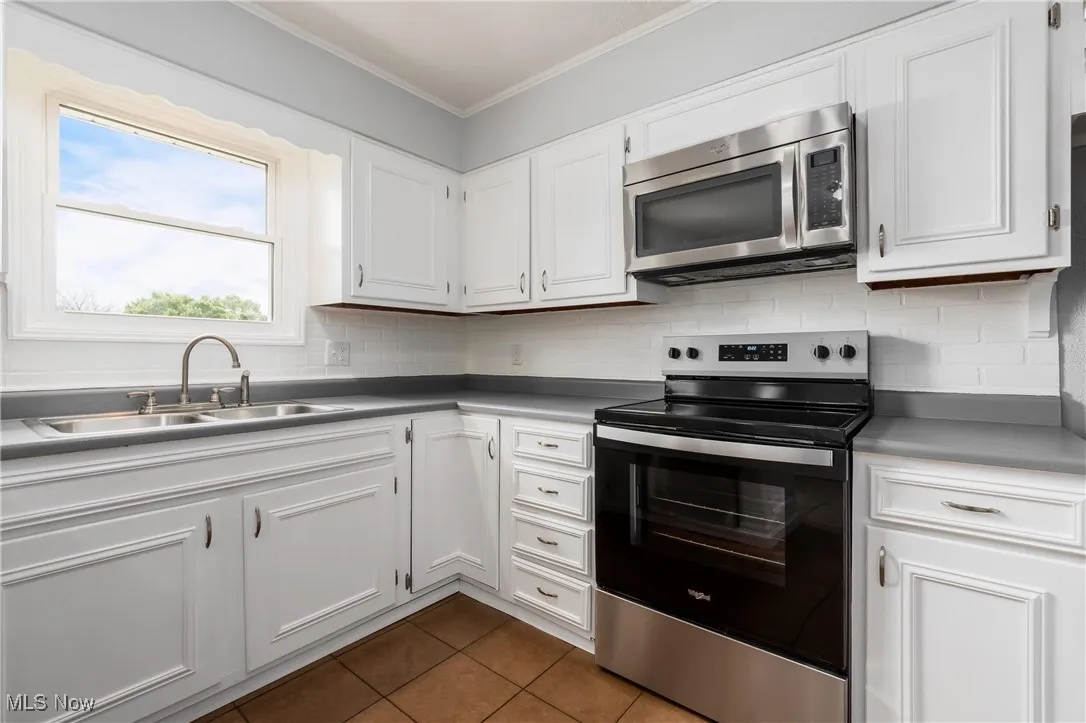 Kitchen with appliances with stainless steel finishes, crown molding, dark tile patterned floors, backsplash, and white cabinetry