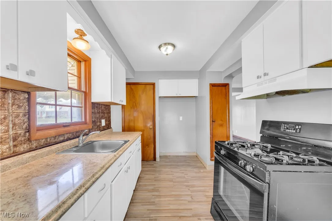 Kitchen featuring black range with gas cooktop, under cabinet range hood, white cabinetry, light wood-type flooring, and decorative backsplash
