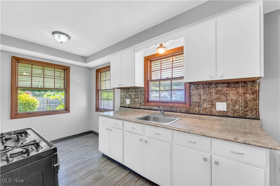 Kitchen featuring black range with gas stovetop, tasteful backsplash, light wood finished floors, and white cabinets