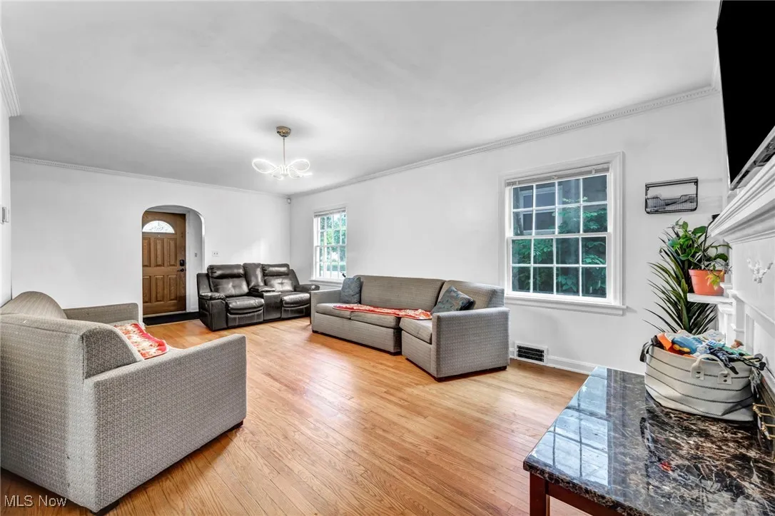 Living area with arched walkways, ornamental molding, a chandelier, and light wood-style flooring