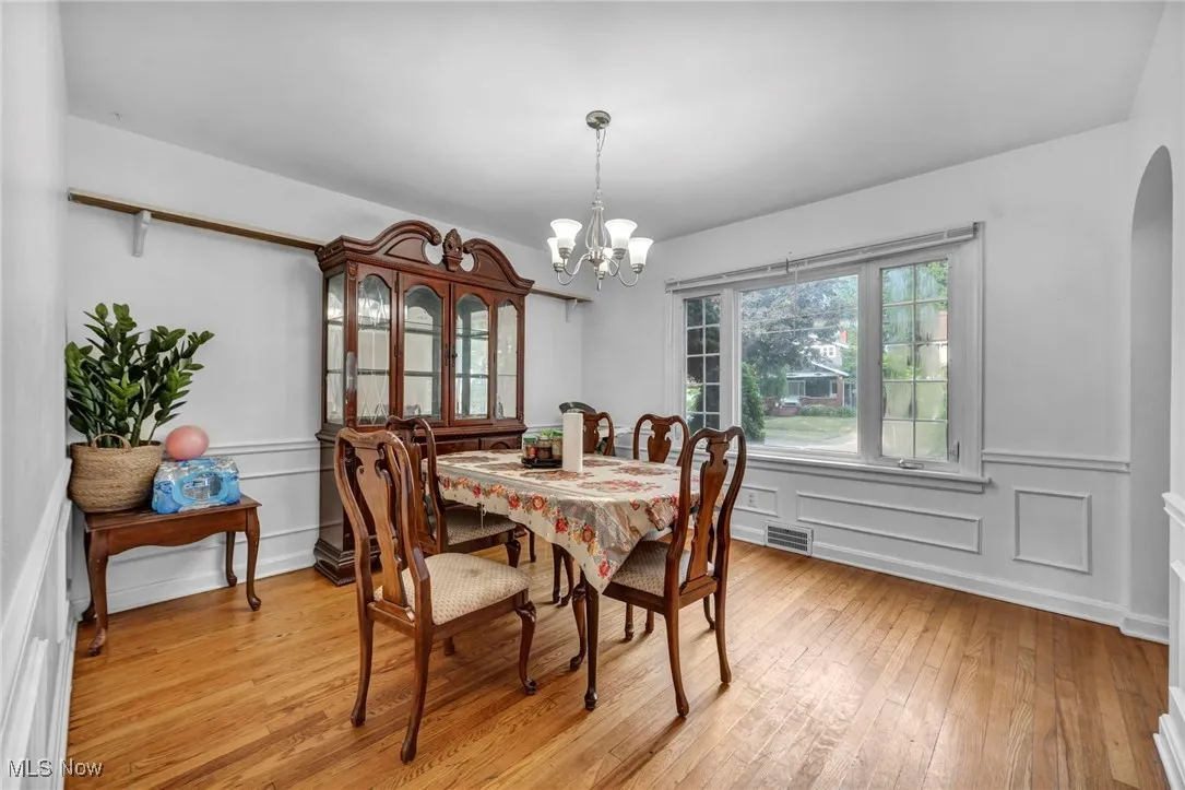 Dining room featuring a chandelier, light wood finished floors, arched walkways, a decorative wall, and wainscoting