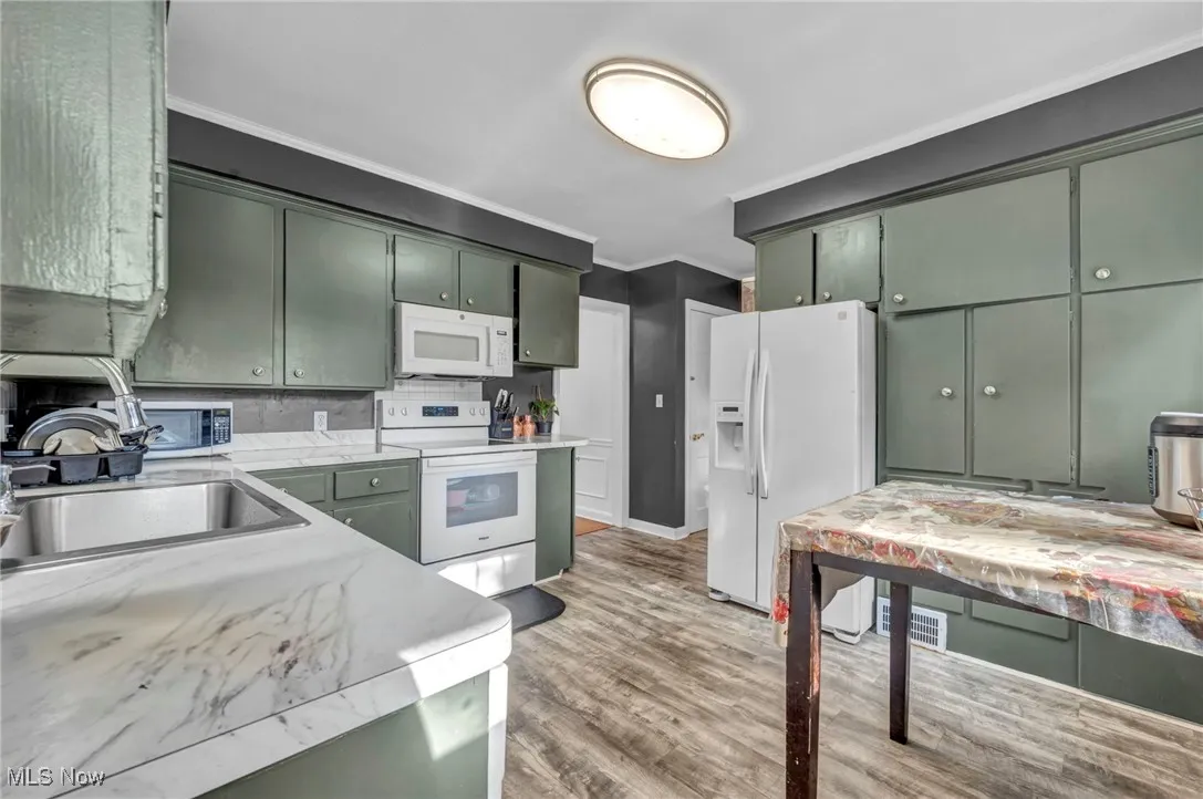 Kitchen featuring white appliances, ornamental molding, light wood-type flooring, green cabinetry, and light stone countertops