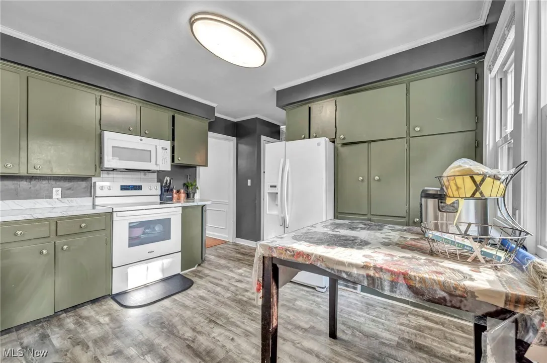 Kitchen with green cabinets, crown molding, white appliances, light wood-style flooring, and light countertops