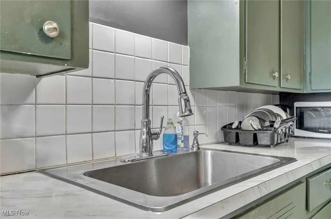 Kitchen view of green cabinets, tasteful backsplash, and light countertops