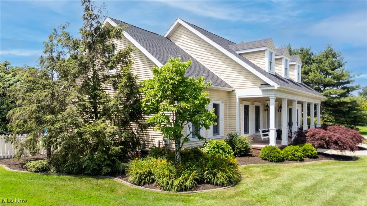 View of property exterior featuring roof with shingles, a yard, covered porch, and lush landscaping