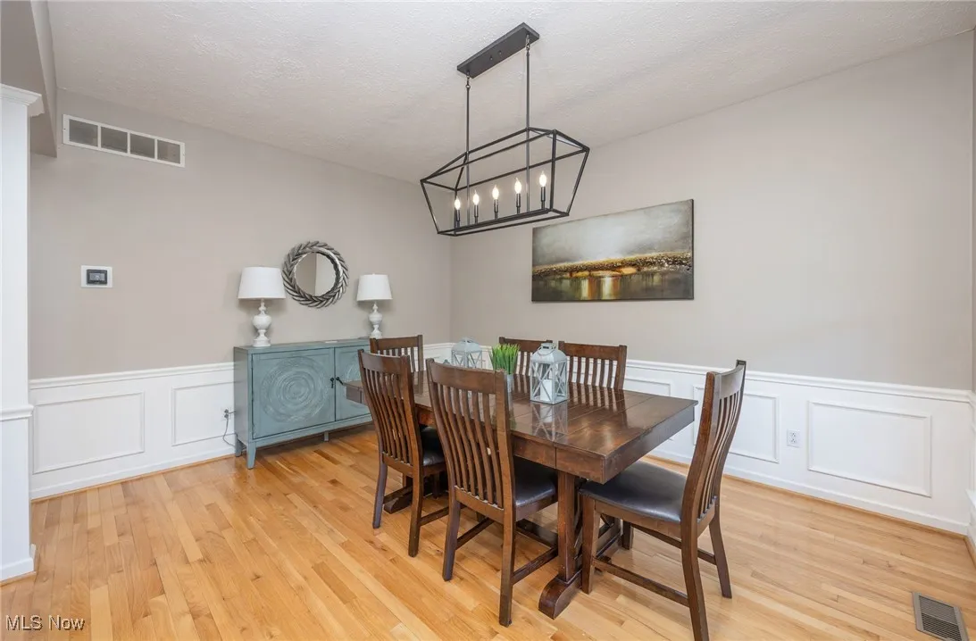 Dining area with light hardwood floors, wainscoting, a decorative wall, and a chandelier