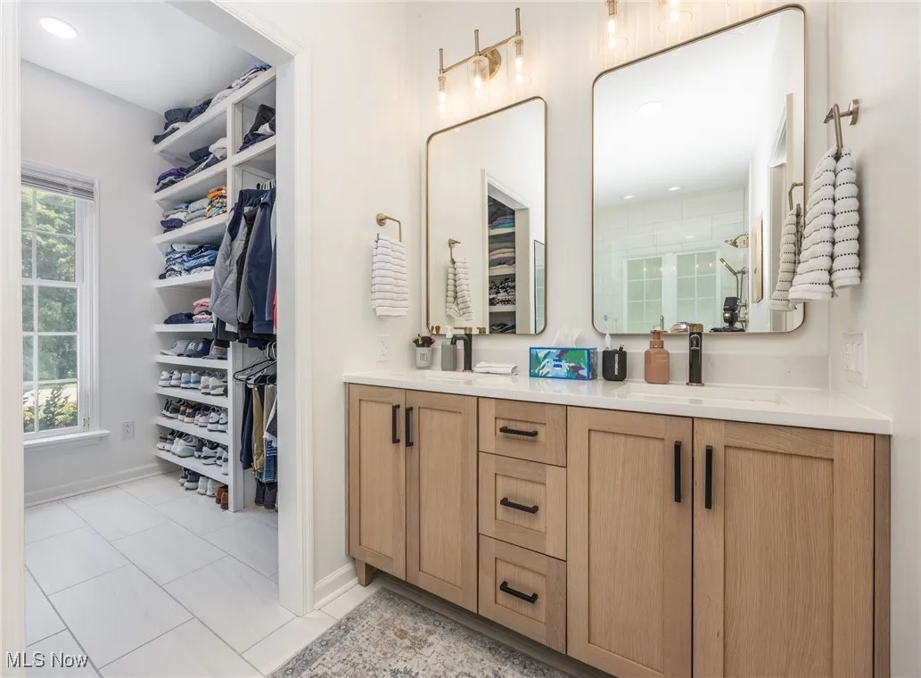 Primary bathroom with double vanity, a tile shower, and a walk in closet