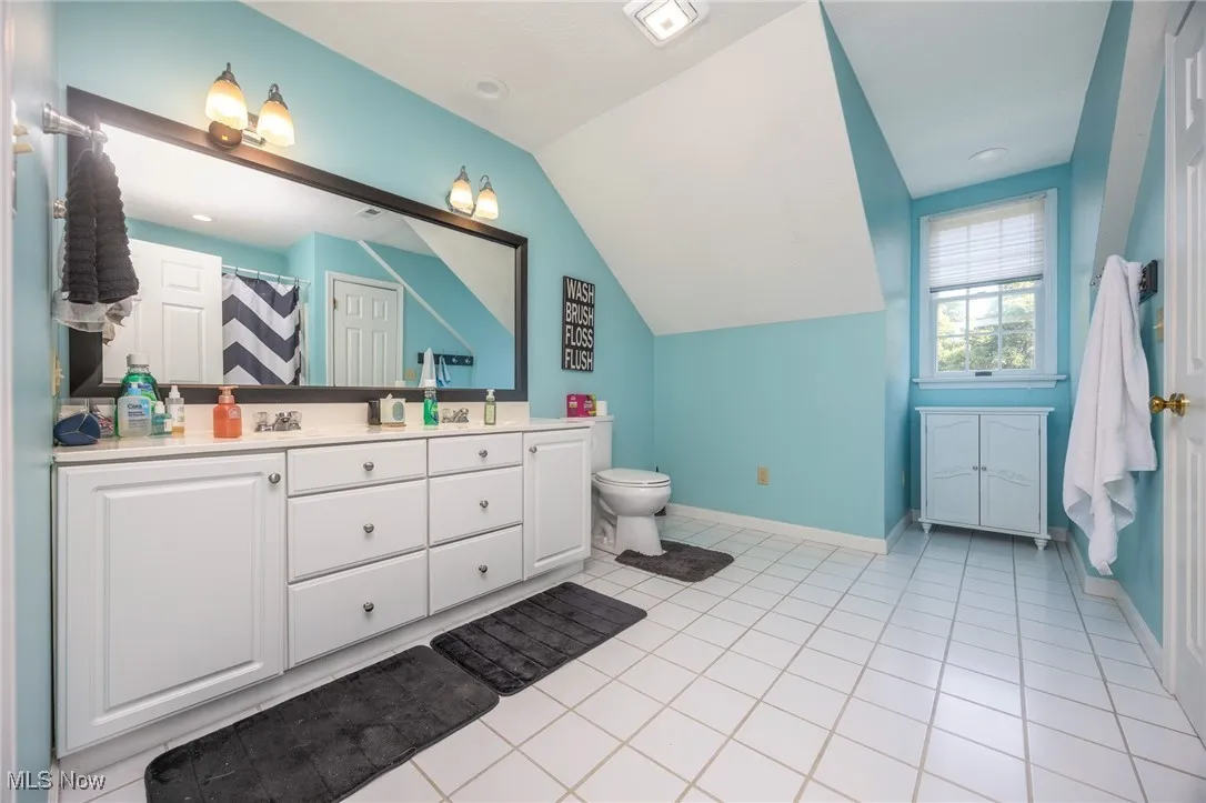 Full bath with double vanity, vaulted ceiling, tile patterned flooring, and a shower with curtain