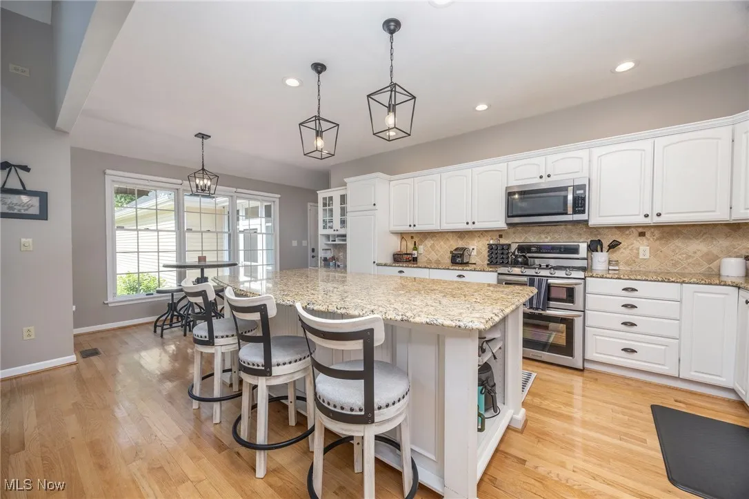 Kitchen with stainless steel appliances, white cabinets, tasteful backsplash, a kitchen bar, and recessed lighting
