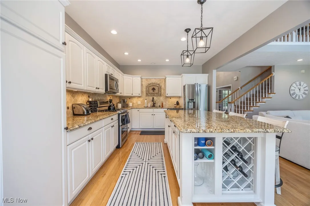 Kitchen with appliances with stainless steel finishes, white cabinets, a kitchen island, light hardwood floors, and recessed lighting