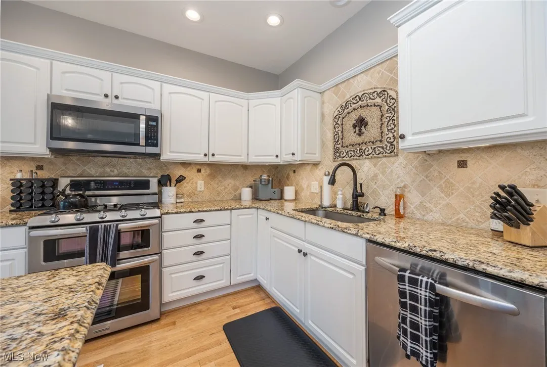 Kitchen with stainless steel appliances, white cabinets, granite countertops, light wood-type flooring, and recessed lighting