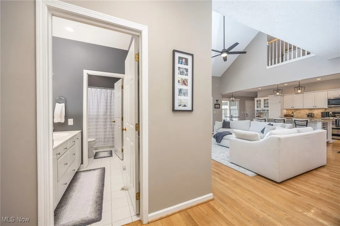 Living area to full bath featuring light hardwood flooring, a ceiling fan, and high vaulted ceiling